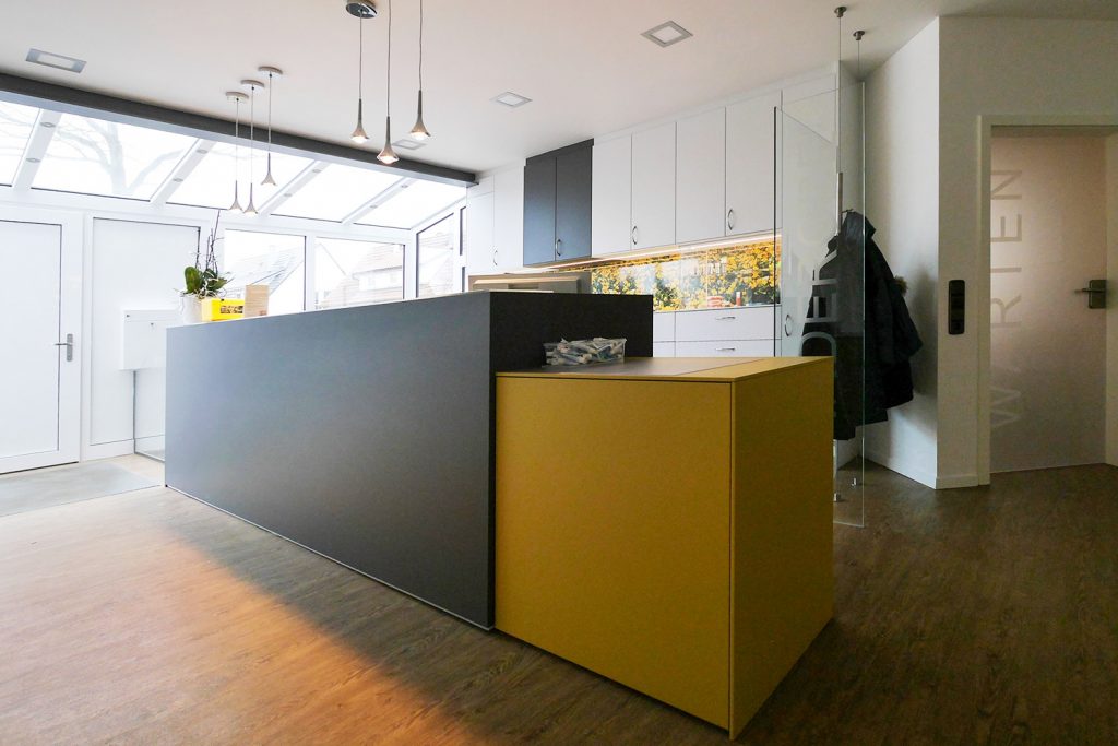 Arbeitsplatz mit Theke und wandhohem Aktenschrank. Beleuchtung der Theke mit Pendelleuchten, weitere Akzentbeleuchtungen in Theke und Schrank integriert.