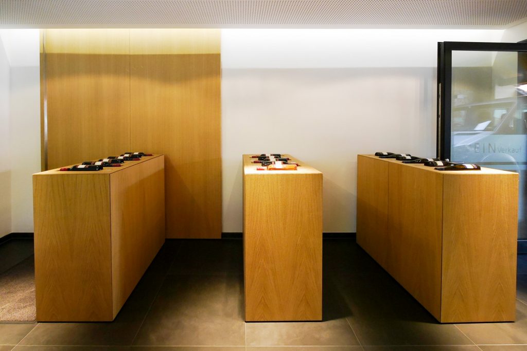 Präsentationskuben mit ausgefrästen Mulden für Weinflaschen und Etiketten. Einseitig Türen auf Gehrung gearbeitet mit griffloser Öffnungstechnik und viel Stauraum.