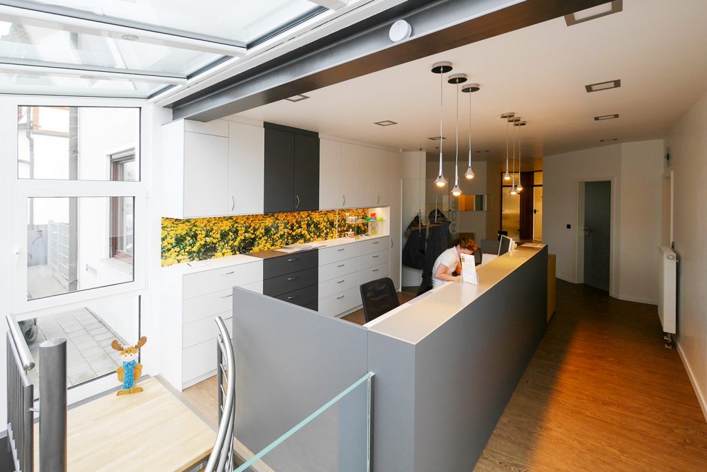 Theke im Empfangsbereich mit zwei Arbeitsplätzen und Aktenschränken. Thekenfront anthrazit lackiert mit Abdeckplatte aus Glas.