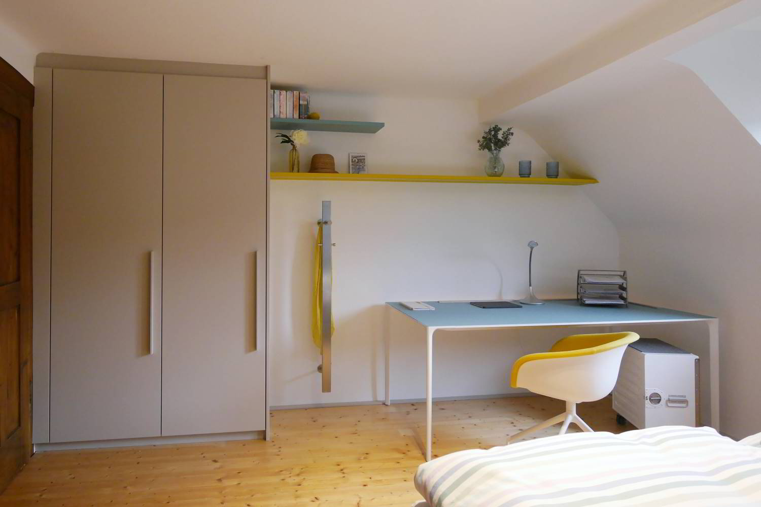 Raum in gelb, türis und hellgrau gehalten. Ein raumhoher Einbauschrank auf der linken Seite, farbige Regalbretter in die Schräge eingepasst und darunter ein Arper Schreibtisch in Kombination mit einer kleinen Bordbar als Bürocontainer.