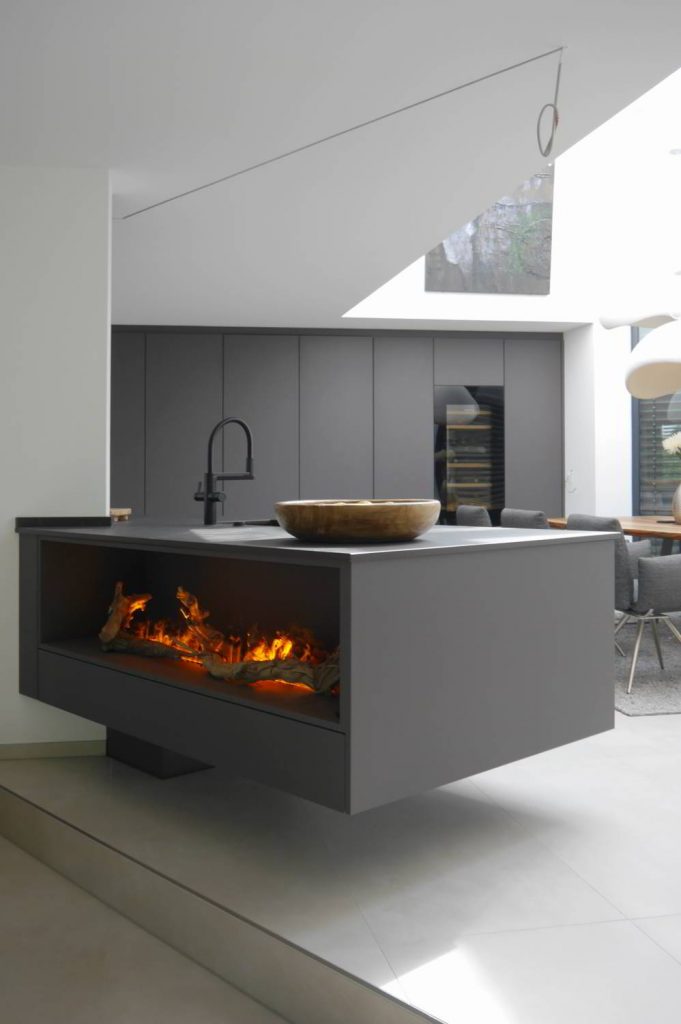 Freischwebende Kücheninseln, hier sichtbar von der Wohnzimmerseite, mit integriertem Elektro-Wasserdampf-Kamen. Im Hintergrund ist die Hochschrankfront zu sehen in einem großen, hohen, offenen Raum