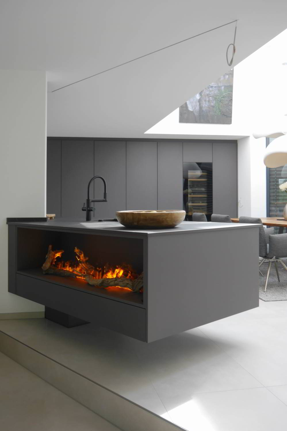 Freischwebende Kücheninseln, hier sichtbar von der Wohnzimmerseite, mit integriertem Elektro-Wasserdampf-Kamen. Im Hintergrund ist die Hochschrankfront zu sehen in einem großen, hohen, offenen Raum