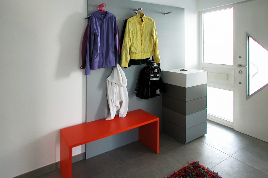 In Grautönen gehaltene Garderobe mit auffallender orangener Bank und einem grifflos zu öffnenden Schrank.