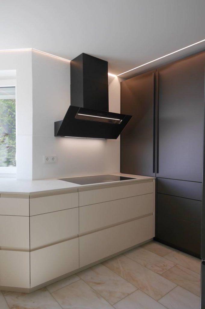 helle Einbauküche mit Griffmulden um die Ecke laufend, Berbel Kopffreihaube darüber und flächenbündig eingelassenes Kochfeld. Im Hintergrund raumhohe Hochschränle in Antrazith Glasoptik