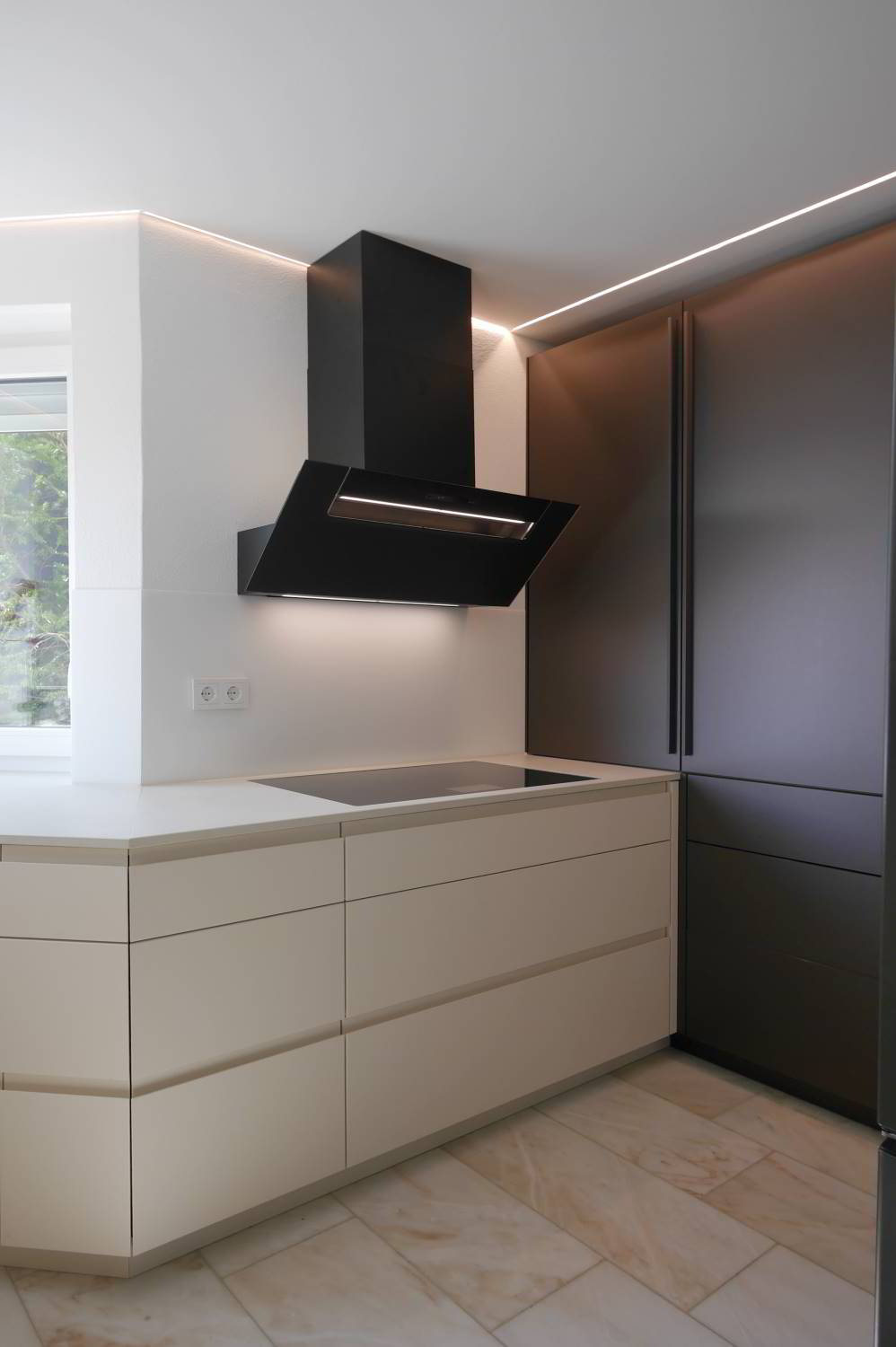 helle Einbauküche mit Griffmulden um die Ecke laufend, Berbel Kopffreihaube darüber und flächenbündig eingelassenes Kochfeld. Im Hintergrund raumhohe Hochschränle in Antrazith Glasoptik