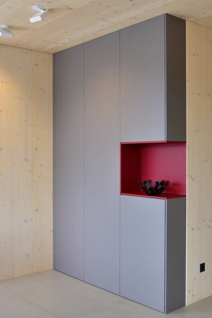 Raumhoher Schrank mit zwei Türen, rechts auch zwei Türen, in der Mitte eine weinrot lackierte Nische. Das Ganze als eine Ecklösung im offenen Wohnraum