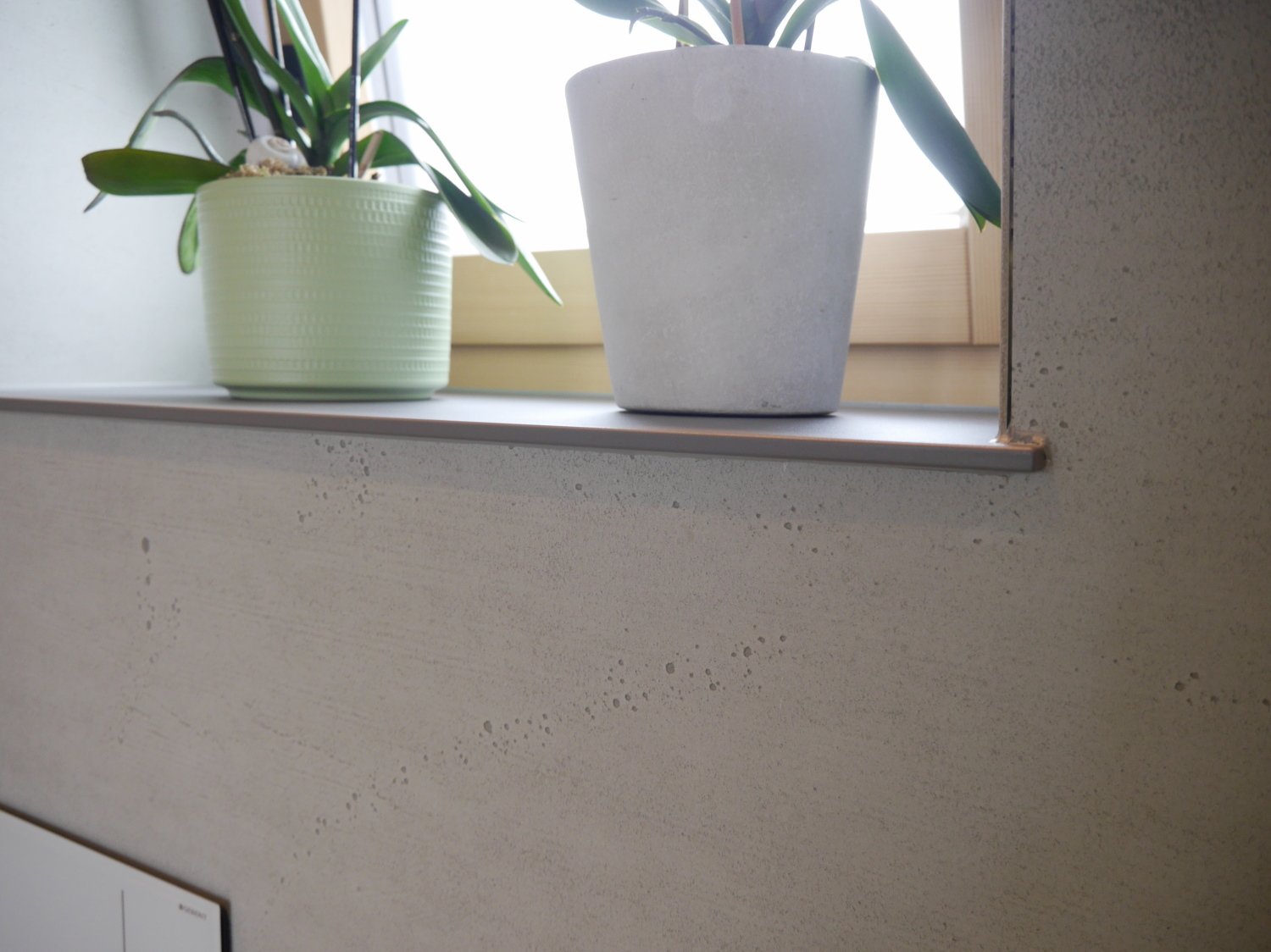 Gezeigt wird ein modernes Badezimmer, mit einem Fenstersims aus Vollkernmaterial in Antrazith gehalten, das gefertigt wurde von der Schreinerei Hartmann WOHNfühlen. Auf den Fenstersims stehen 2 Blumentöpfe.