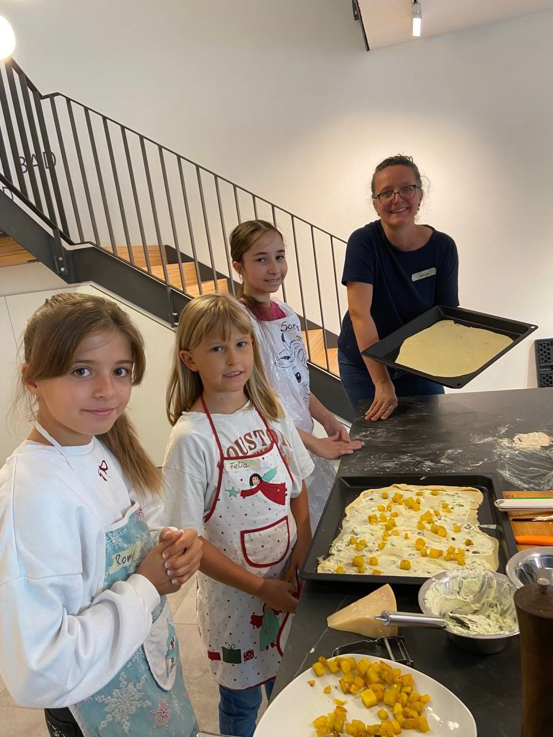 Kinderkochkurs in der Ausstellung der Schreinerei Hartmann WOHNfühlen, mit drei Kindern beim Belegen des Flammkuchens und Tanja Koch mit einem Flammkuchenteig auf dem Blech in der Hand