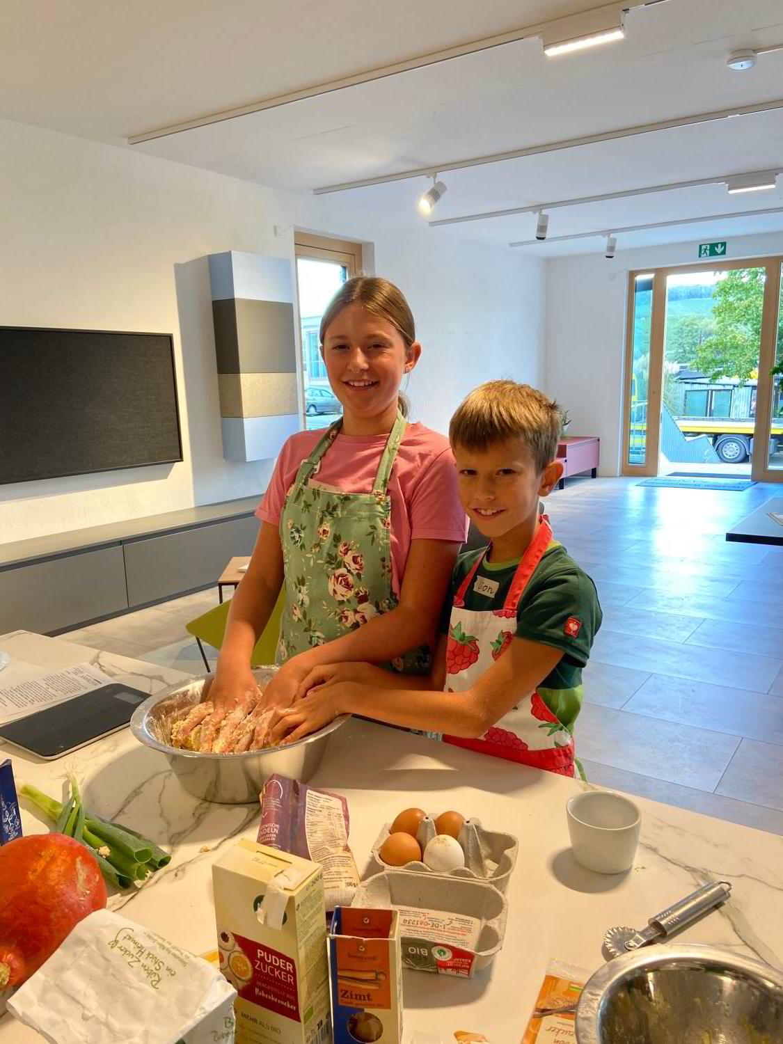 Zwei Kinder mit Schürze beim Kneten eines Teiges in der Ausstellung der Schreinerei Hartmann WOHNfühlen an einer weißen Arbeitsplatte