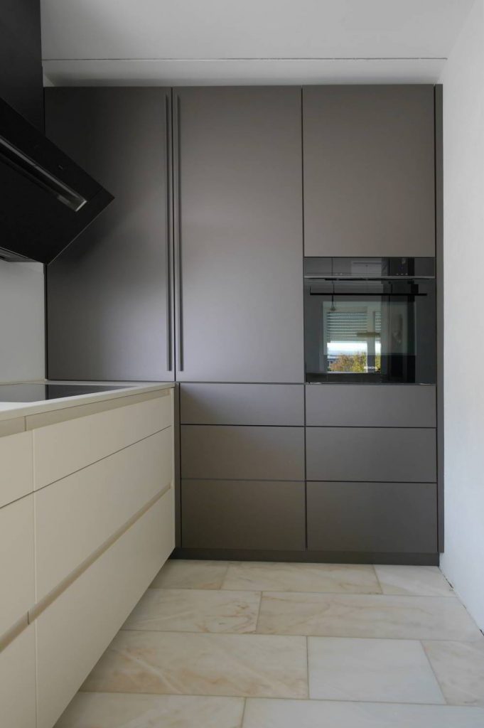 Einbauküche mit raumhohen Hochschränken in Rauvisio Glaslaminat Tericcio matt, links Unterschränke in hell mit Griffmulden