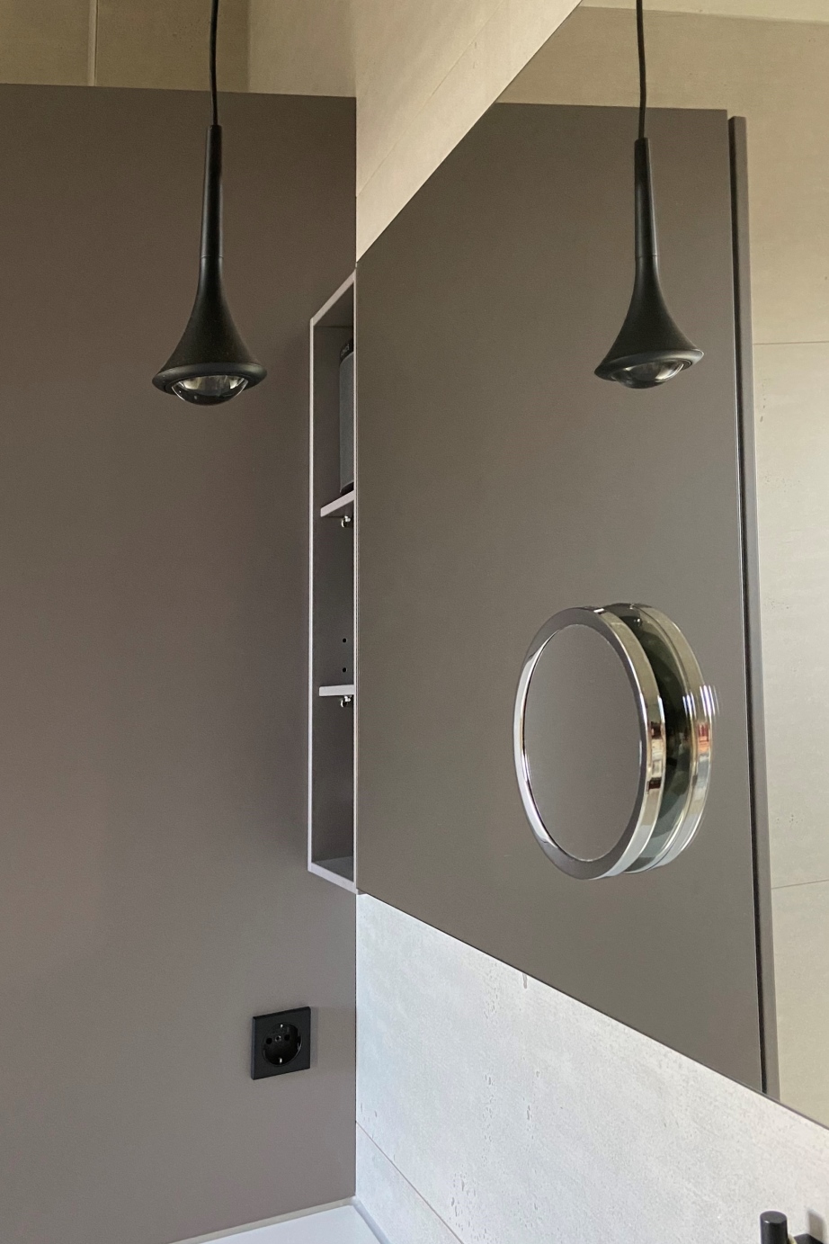 Ein stilvoller Spiegel an der Wand, ergänzt durch ein offenes Regal in Grau und eine elegante Pendelleuchte in Schwarz ist eine individuelle Planung für ein Badezimmer.