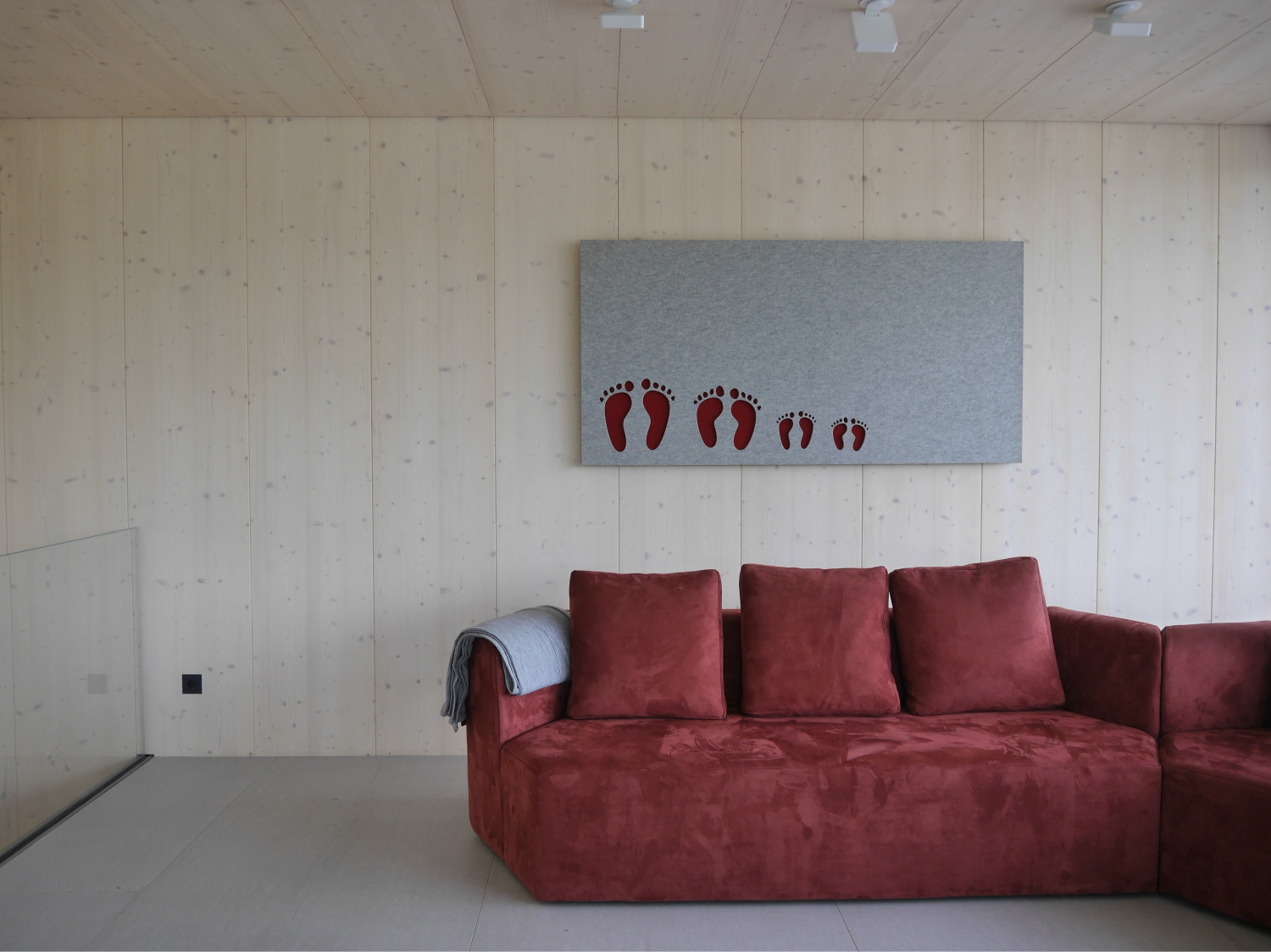Eine kreative Einrichtungsidee für das Wohnzimmer. Ein rotes Sofa vor einer Wand aus Fichtenholz auf Boden in imi-Beton. Modernes Wohnen mit Hartmann WOHNfühlen Ellhofen.