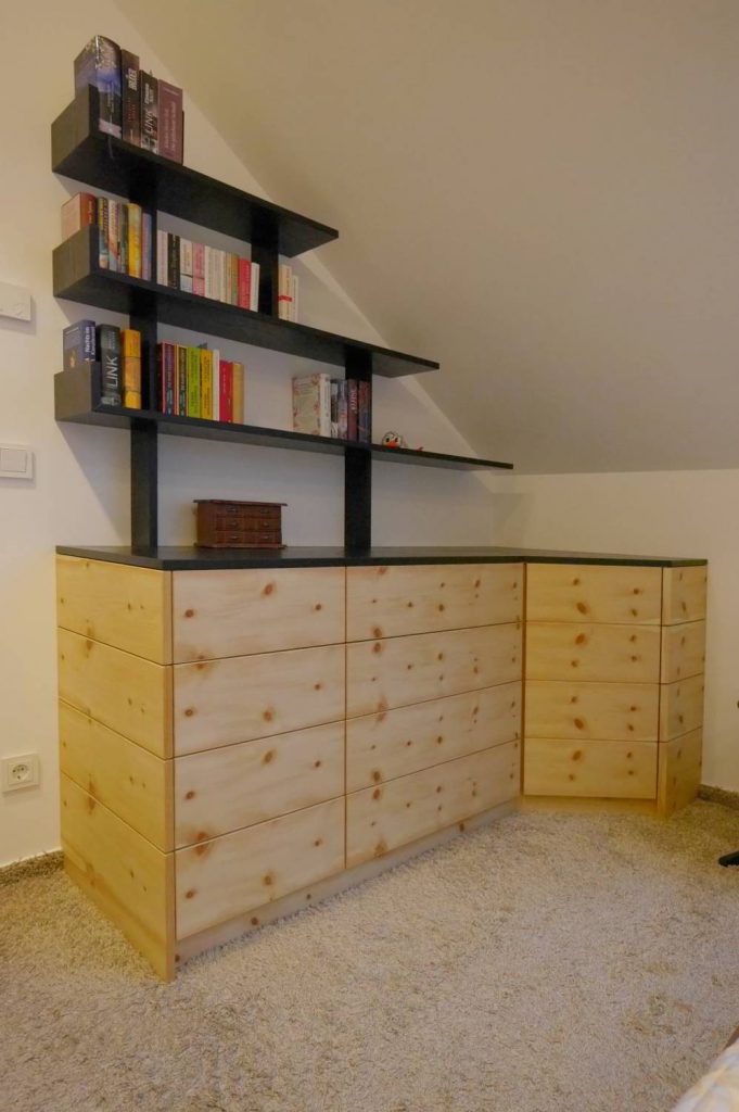 Sideboard über Eck laufend in Zirbe furniert, Abdeckplatte und aufgesetztes Regal in dunkel. Das ganze steht in einer Raumecke mit Dachschräge.