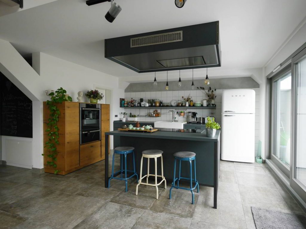 Anthrazitfarbene Einbauküche mit freistehendem Element, in dem sowohl das Kochfeld als auch eine Sitztheke untergebracht ist. Als Kontrast dient ein Holzelement, in dem weitere Geräte untergebracht sind.