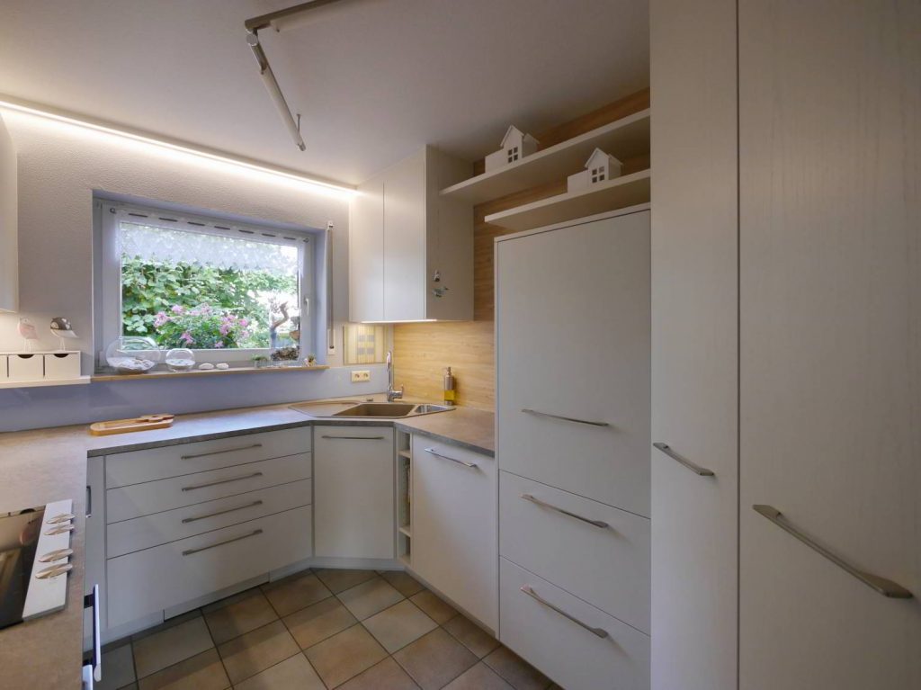 Einbauküche in schlichtem weiß mit Eckspüle, einseitiger Holzrückwand und hellbllauer Glasrückwand.
