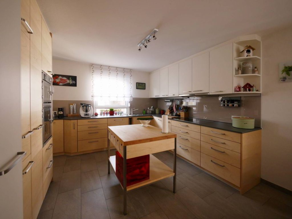 Helle Holzeinbauküche mit freistehendem Element und dunkler Arbeitsplatte. Weiße Hängeschränke und Metallgriffe.