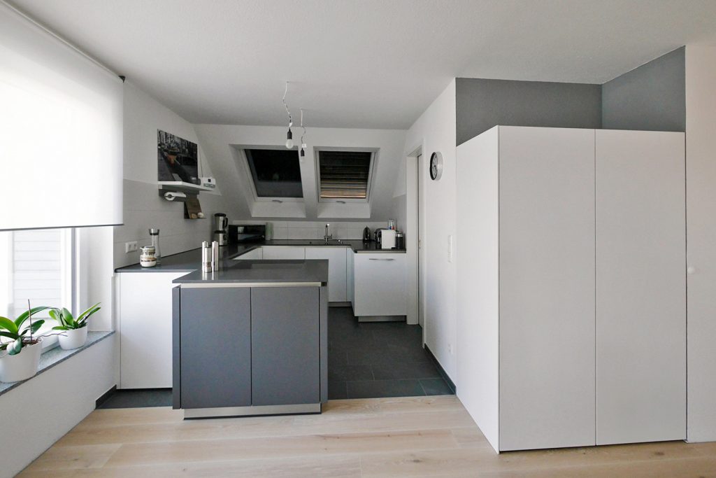 DG-Einbauküche mit weißen und anthrazitfarbenen Elementen. Großer griffloser Einbauschrank im Eingangsbereich bietet noch mehr Stauraum.