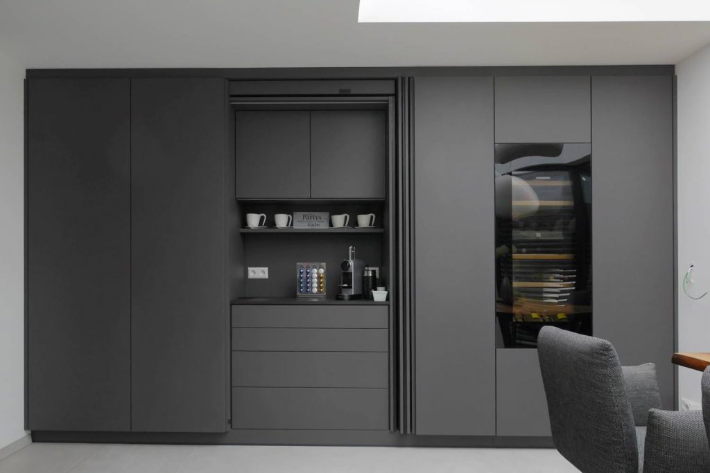 Hochschrankfront in Antrazit gehalten, mit Revego-Türe im linken Bereich integriert, die geöffnet ist. Hier ist die Kaffeebar zu sehen. Im Anschluss verschiedene Hochschränke und ein Weintemperierschrank. Alles bündig in die Wand eingebaut.