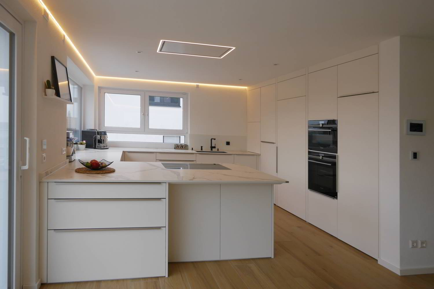 hell gehaltene Küche, mit flächenbündig in die Decke eingelassener Dunstabzugshaube von Novy. LED Beleuchtung in den Raumecken und Hochschränke bis an die Decke