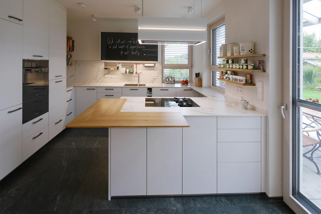 Offene weiße Einbauküche mit schwarzen Griffen und Holzelementen.