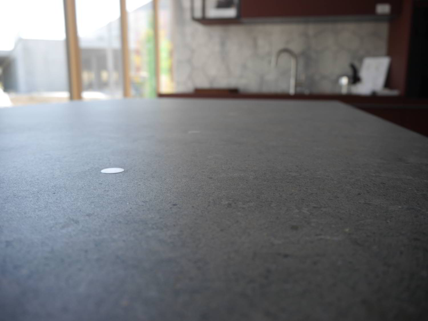 silbener metallischer Punkt auf der Dekton Arbeitsplatte. Im Hintergrund Ausstellung von Hartmann WOHNfühlen in Elhofen mit einer Küche in weinrot.