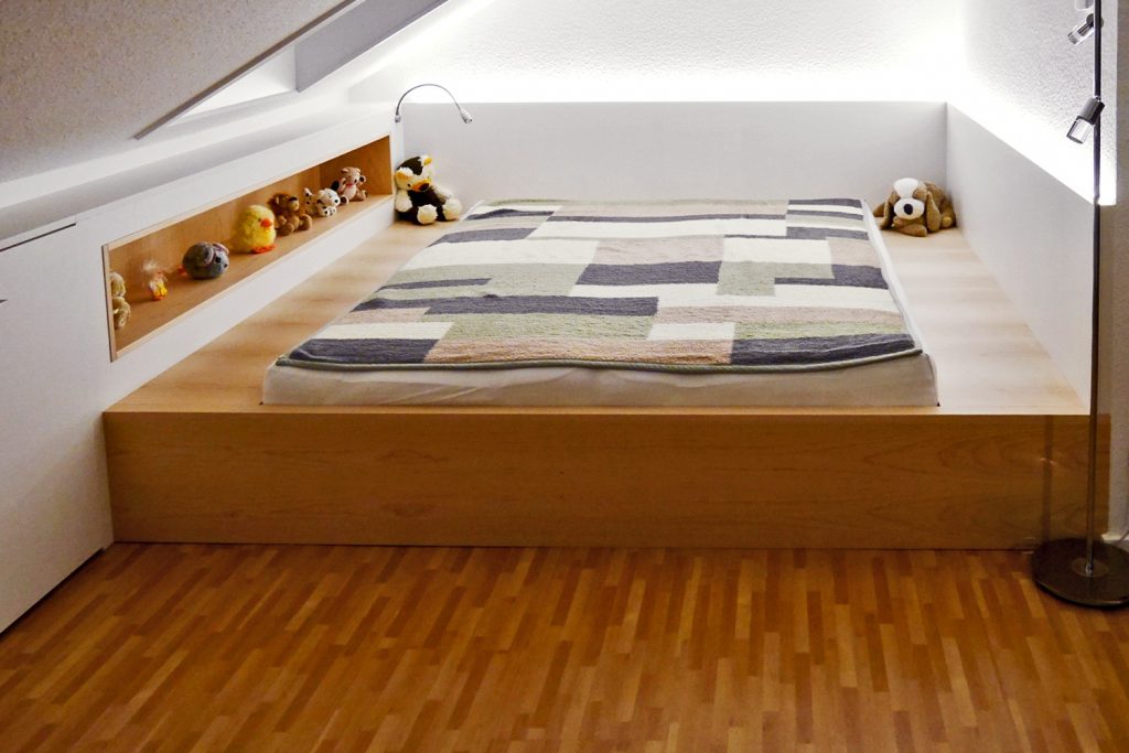 In Dachschräge eingepasstes Bett mit eingebauter Büchernische und LED-Beleuchtung.