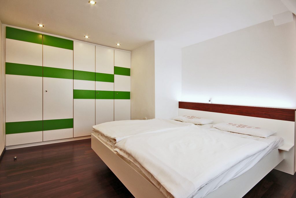 Schlafzimmereinrichtung in weißem und apfelgrünem Mattlack sowie Holzapplikation in Olivenbaum Dekor. Kopfteil mit flächenbündig eingearbeiteter LED-Beleuchtung