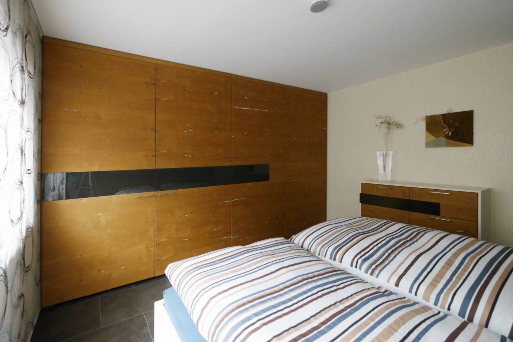 Viertüriger Kleiderschrank mit flächenbündigen Schiebetüren aus Eiche Furnier mit weiß ausgespachtelten Ästen und Rissen und einem dunklen Streifen als Akzent.