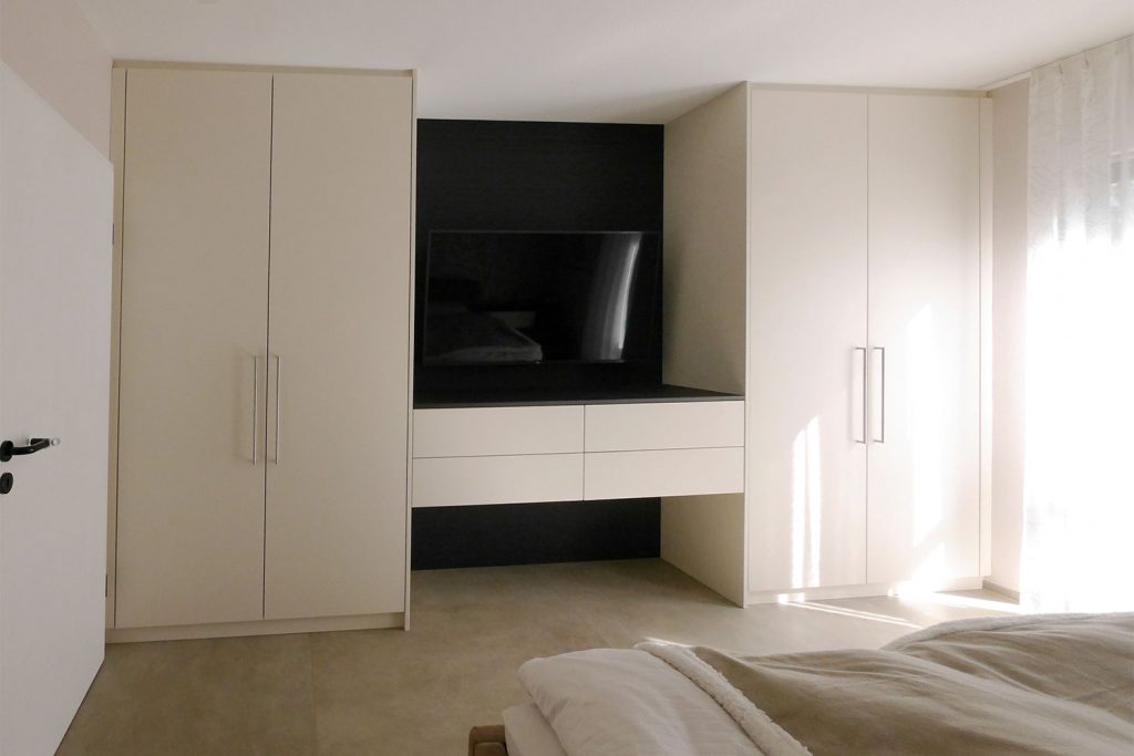 Zwei weiße separate Kleiderschränke in der Mitte verbunden durch wandhängendes Board mit Schubladen, gefertigt vom Schreiner.