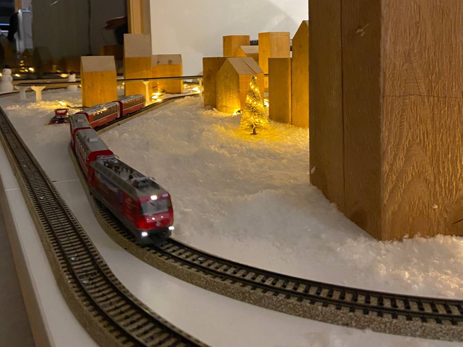 Modellbahn, rot in Schneelandschaft mit beleuchtetem Tannenbaum und massiven Holzhäusern