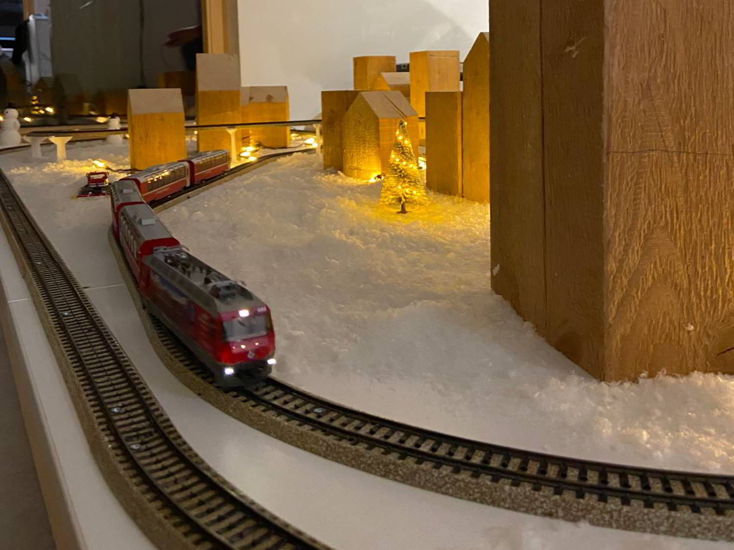 Modellbahn, rot in Schneelandschaft mit beleuchtetem Tannenbaum und massiven Holzhäusern in der Ausstellung von Hartmann WOHNfühlen.
