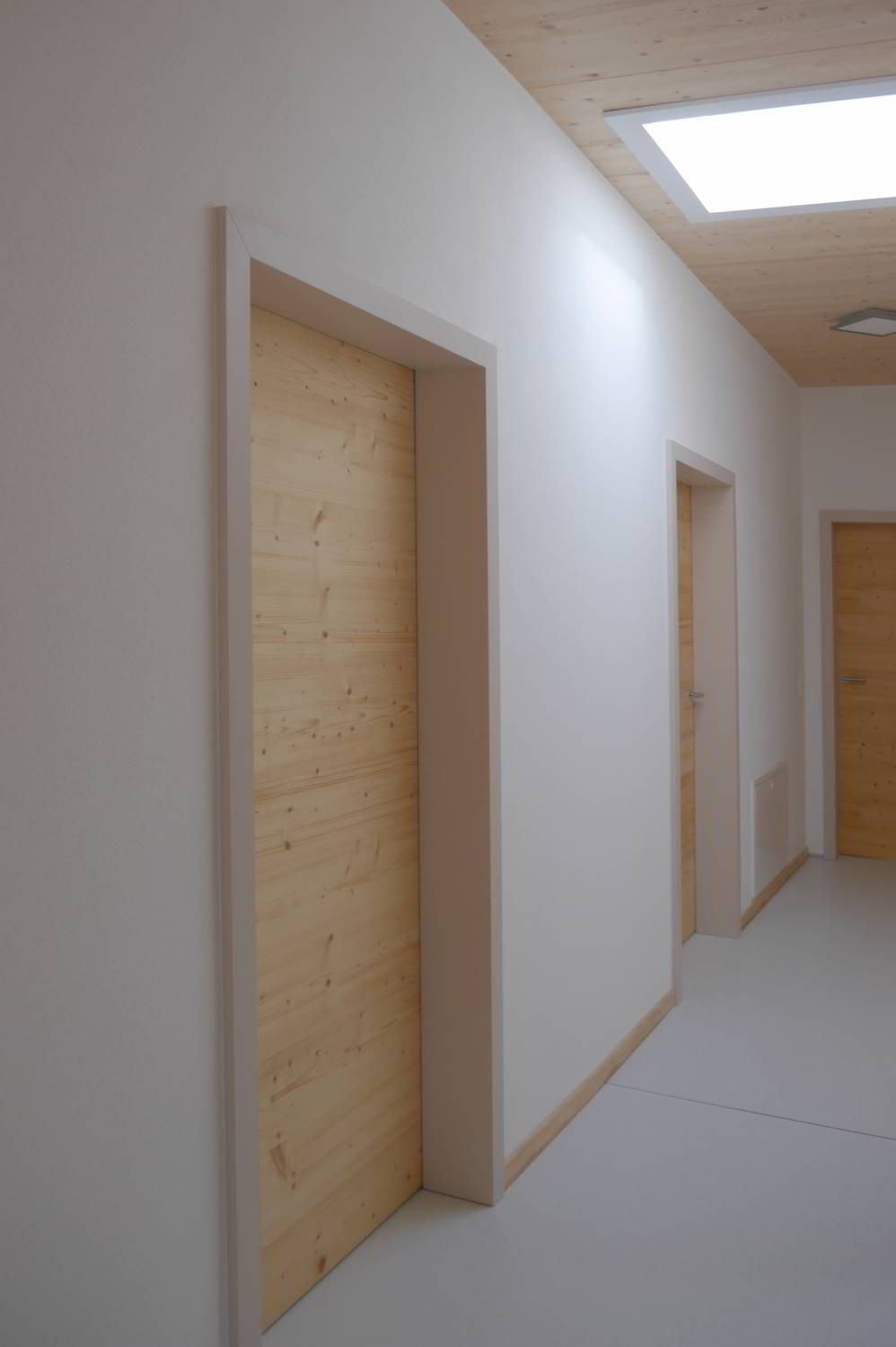 Flur mit weißen Wänden. Im Flur mehrere Türen abgehend. Zargen in einem hellen beige ton lackiert und Fichte Türeblätter.