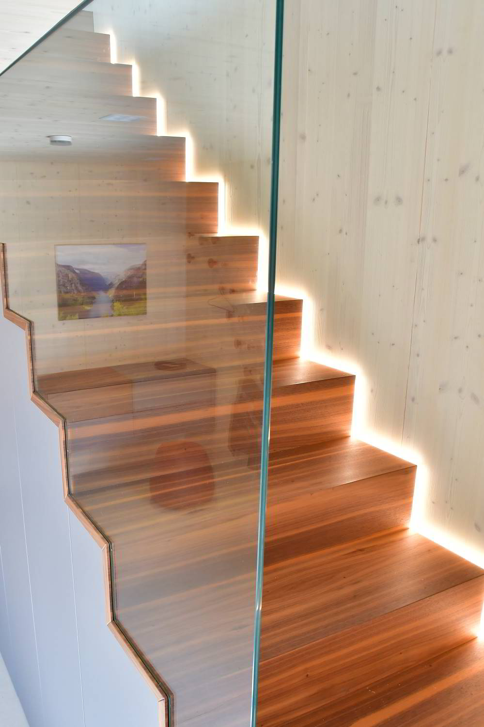 Die nussbaum furnierte Treppe mit eingearbeitetetm LED-Streifen, Holzwand im Anschluss. Möbelberatung bei Hartmann WOHNfühlen Ellhofen in der Ausstellung.