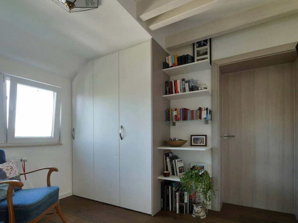 An die Wand und die Dachschräge eingepasster Schrank mit drei Türen.