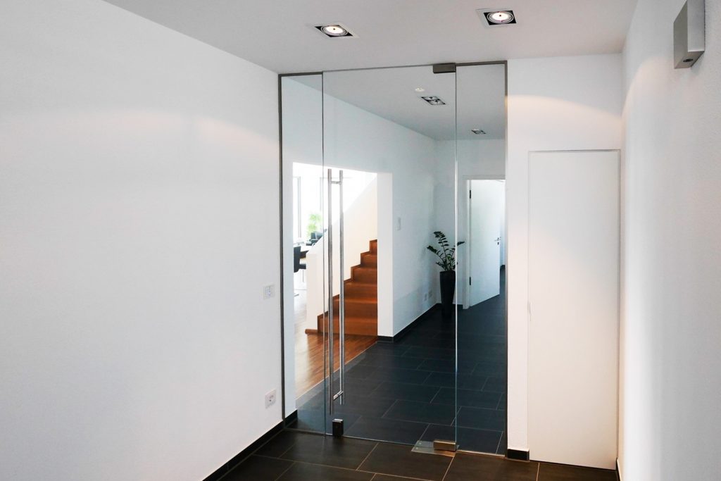 Windfang mit Ganzglas-Pendeltüre und zwei feststehenden Seitenteilen aus ESG Klarglas, inklusive ein zum Boden verriegelndes Schloss